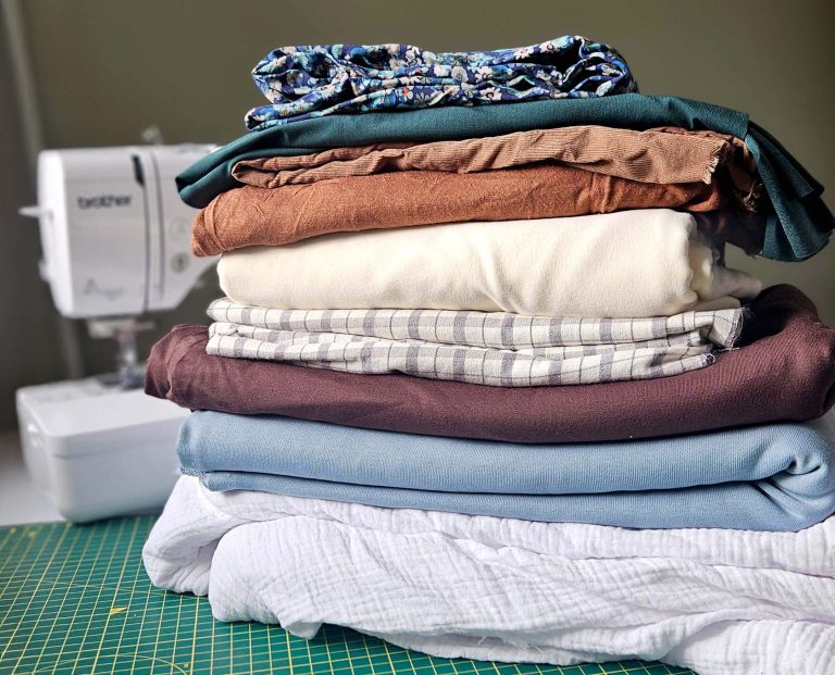 A pile of dressmaking fabric sat on top of a cutting mat, with a sewing machine in the background.